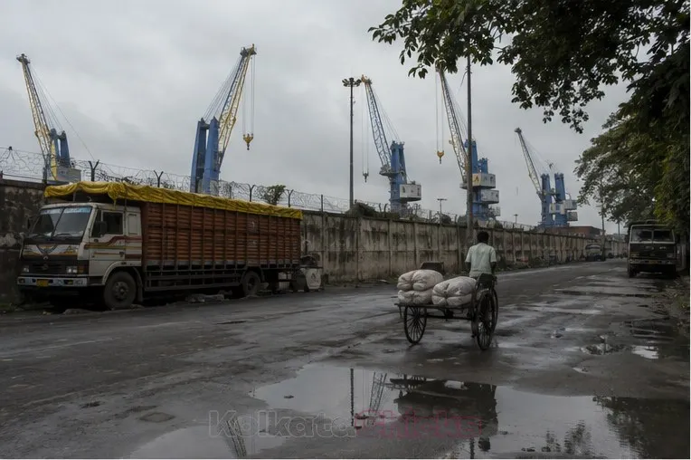 A wet road near the Kidderpore docks in Kolkata, with port cranes behind the wall