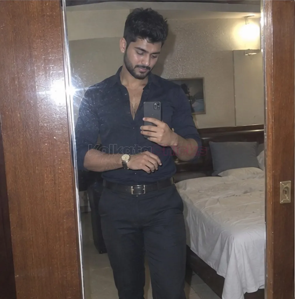A man in a dark shirt getting ready at a hotel room mirror in Kolkata