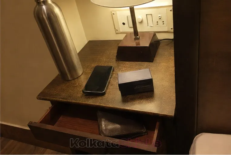 A hotel bedside table at night with a water bottle, a phone and a small box